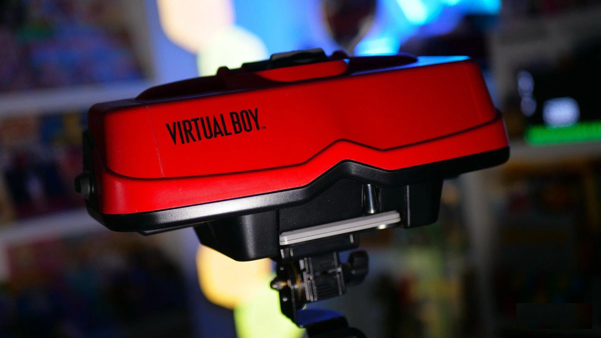 A close-up of a red Nintendo Virtual Boy gaming console on a stand, with a blurred colorful background.