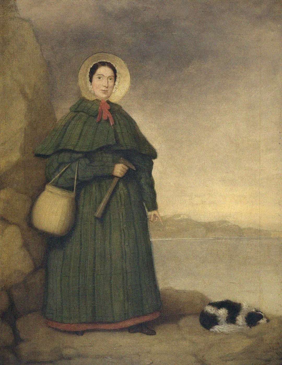 A woman in a green cloak and bonnet stands on a rocky shore, holding a telescope and a bag. Beside her, a black-and-white dog lies curled up, with a cloudy sky and distant hills in the background.