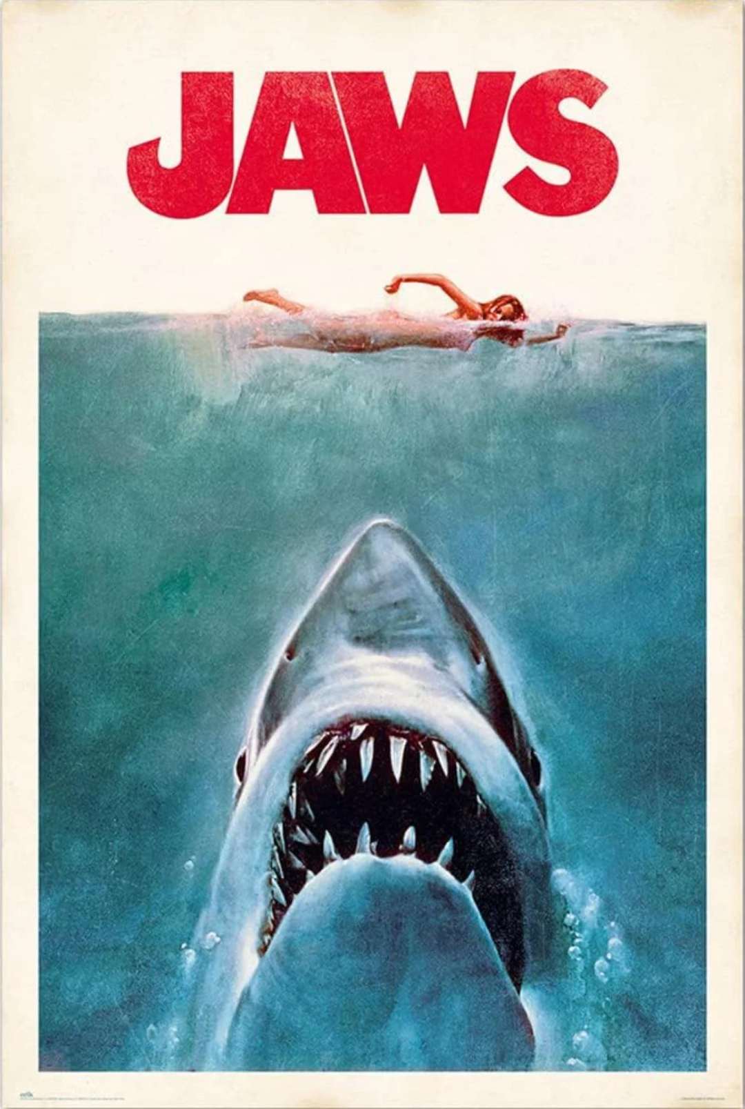 A swimmer on the surface of the water above a large shark with its mouth open wide, swimming upward. The word "JAWS" appears in bold red letters at the top of the image.