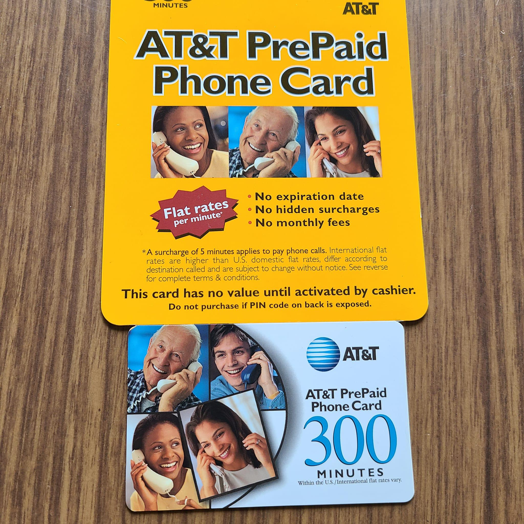 Two AT&T prepaid phone cards on a wood surface. The top card is yellow with usage details, while the bottom card is blue and white with "300 minutes" and photos of people talking on phones.