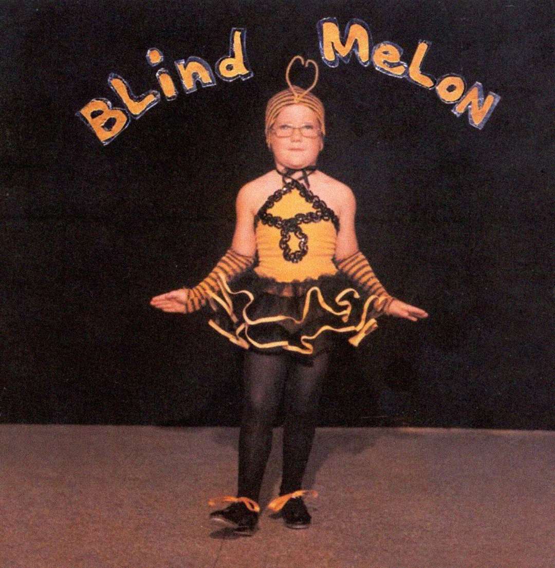 A child in a yellow and black bee costume stands with arms outstretched in front of a dark backdrop. Above, "Blind Melon" is written in playful yellow letters.