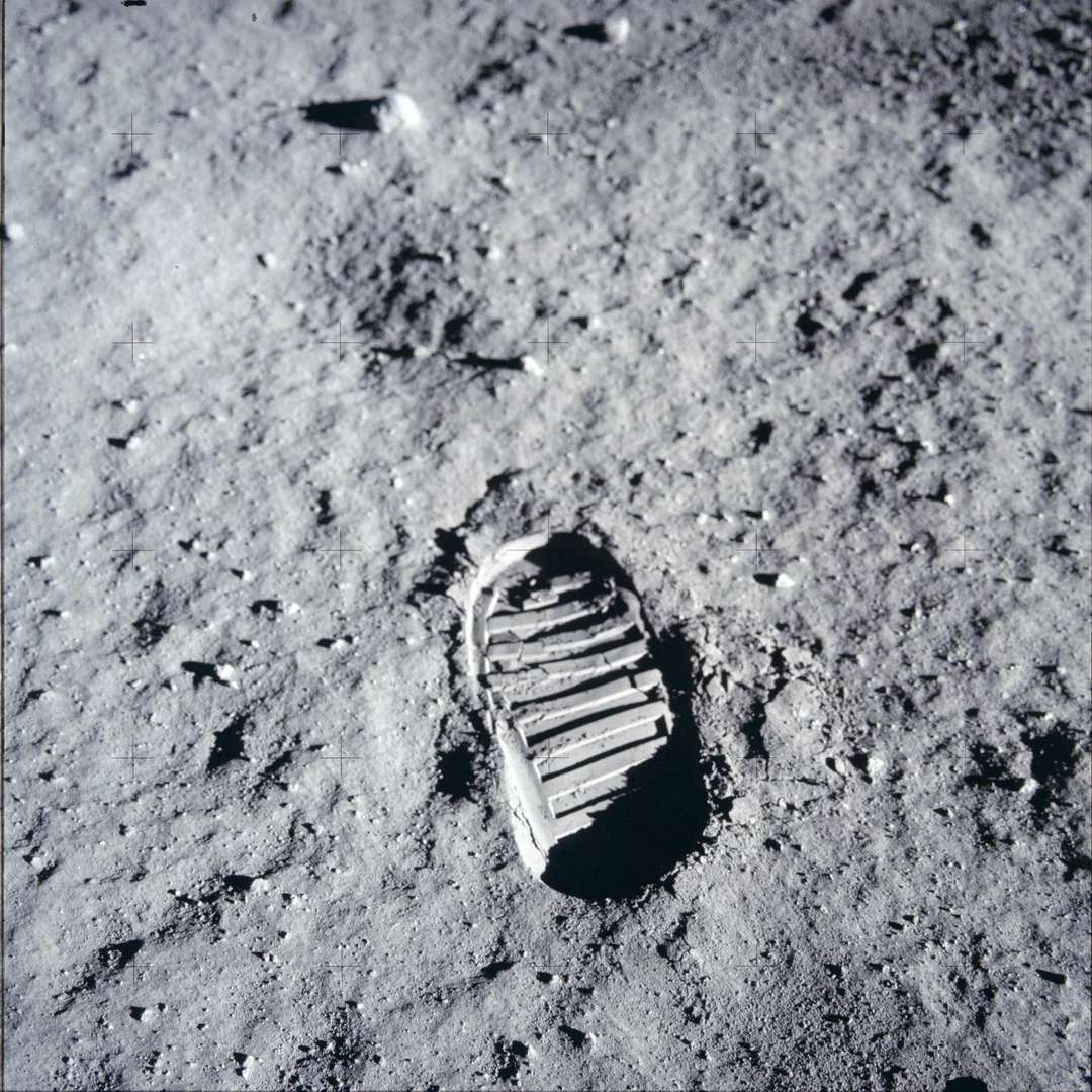 A single astronaut's boot print is clearly visible on the dusty, gray lunar surface, surrounded by small rocks and textured soil.