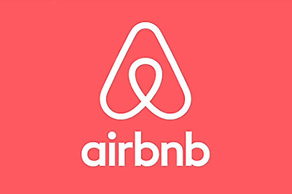 Airbnb logo featuring a white abstract symbol above the word "airbnb" in lowercase white letters, all set against a coral pink background.
