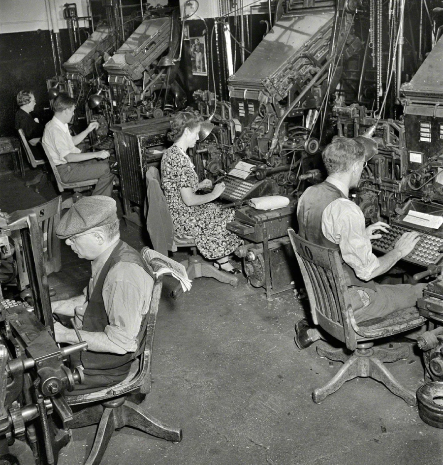 Several men and a woman sit at large, mechanical typesetting machines in a busy, vintage print shop, focused on their work. The room is filled with industrial equipment and worn wooden chairs.