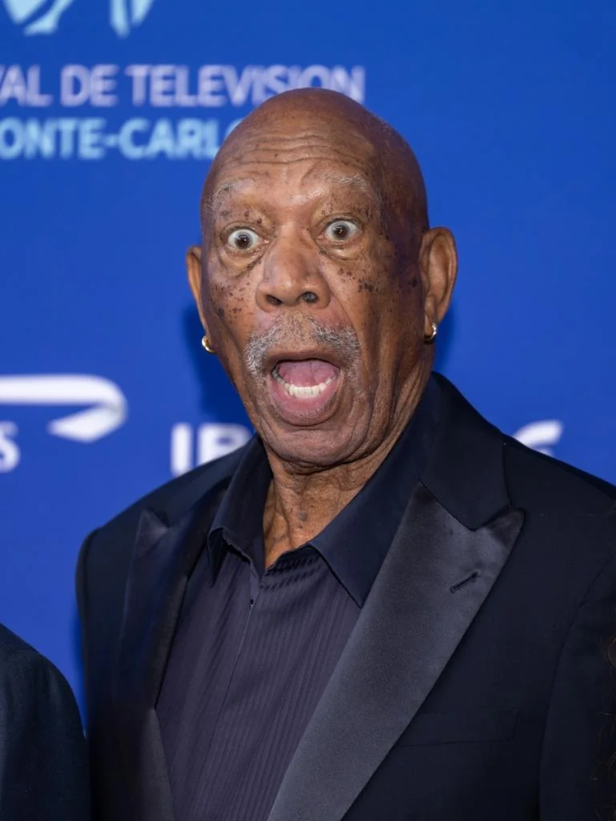 An older man in a black suit stands in front of a blue backdrop, looking surprised with wide eyes and mouth open. The backdrop has white text and logos related to a television festival.