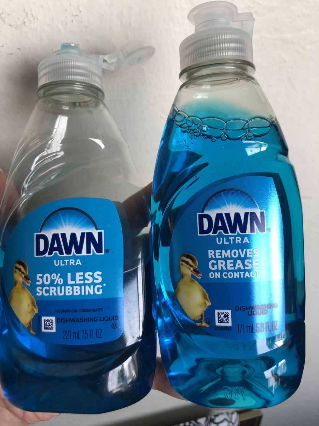 Two bottles of Dawn Ultra dishwashing liquid, one labeled "50% Less Scrubbing" (221 mL) and the other "Removes Grease on Contact" (571 mL), both with blue liquid and a duck image on the label.