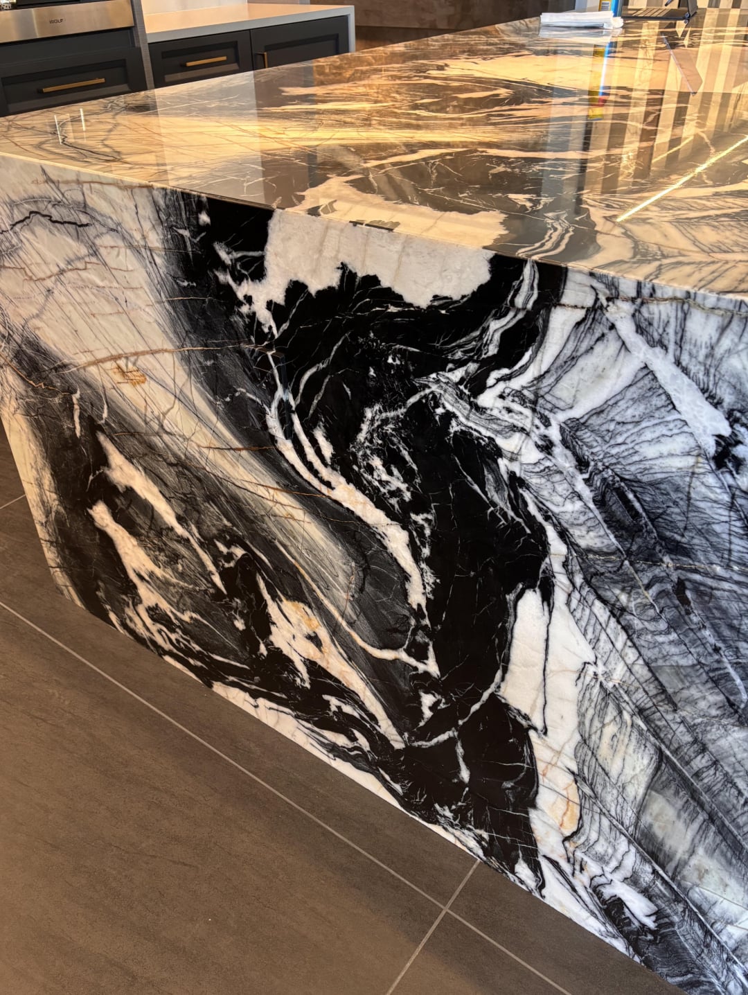 A close-up of a kitchen island featuring a dramatic black and white marble pattern with swirling, bold veining, set against a modern floor and cabinetry.