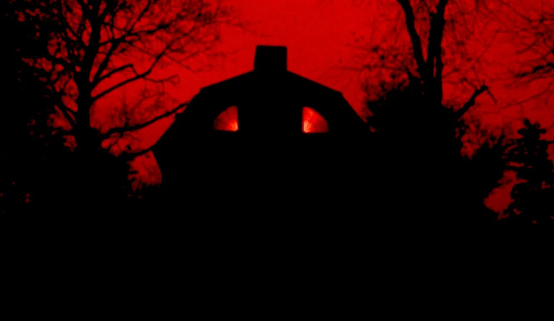 A dark, shadowy house with two glowing windows resembling eyes stands against a vivid red sky, surrounded by bare trees, creating a spooky and eerie atmosphere.