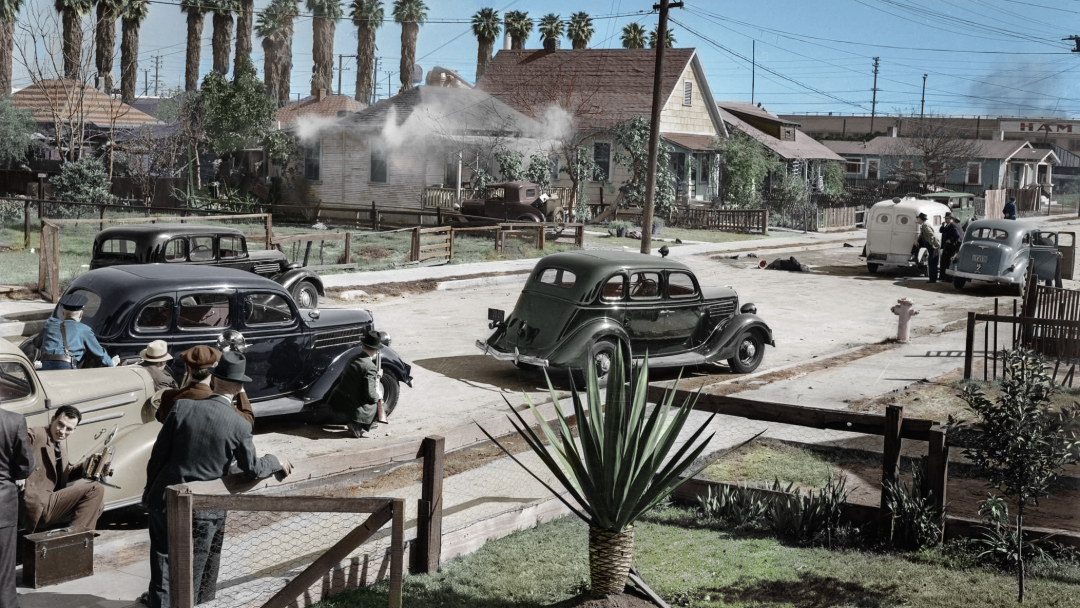 A vintage street scene shows 1930s cars and people in hats gathering on a sunny day. Smoke rises from a house, palm trees line the background, and power lines crisscross above wooden homes and gardens.