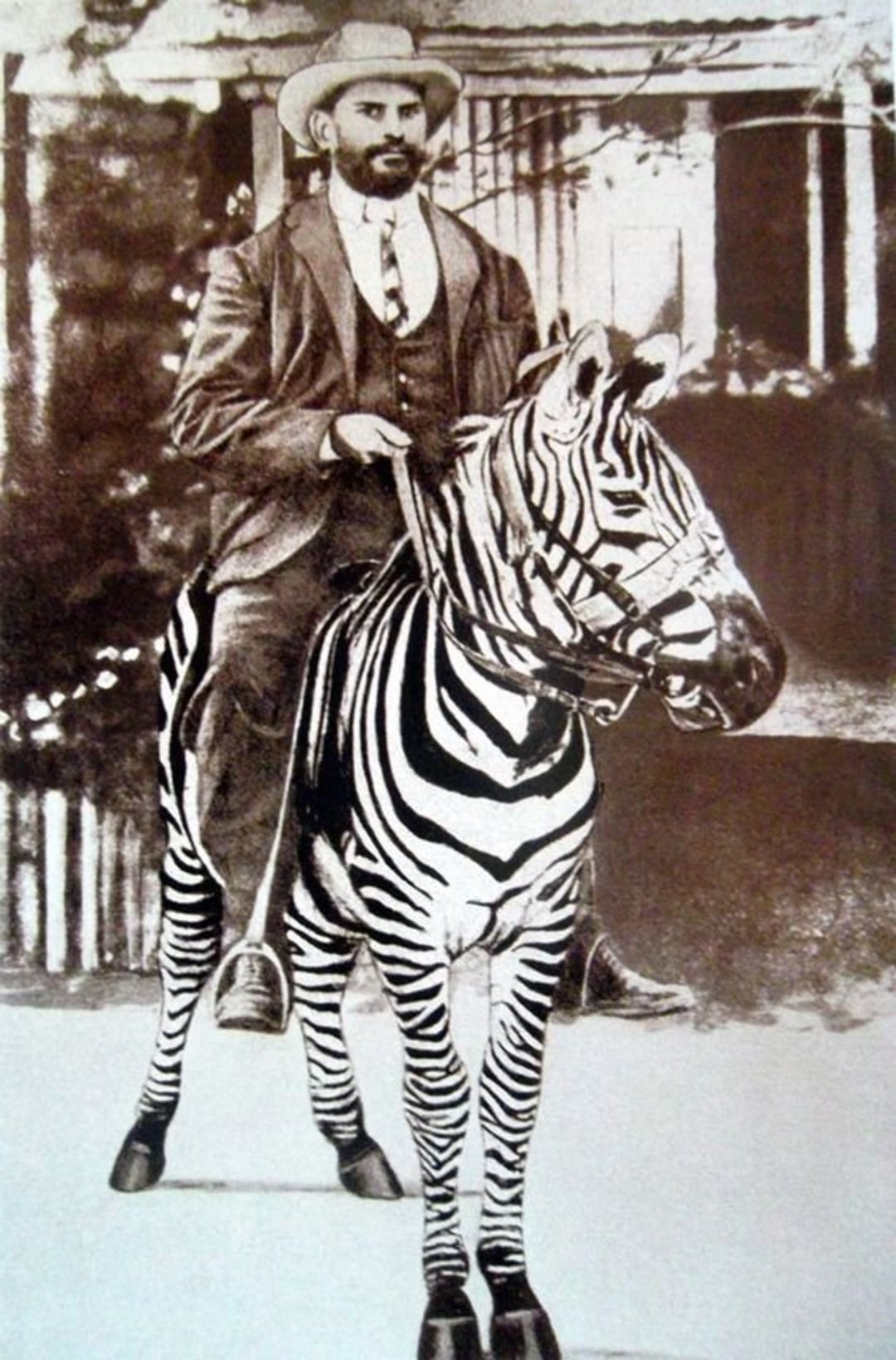 A man in a suit and hat rides a zebra down a street; the image has a sepia tone, giving it an old-fashioned, vintage appearance.