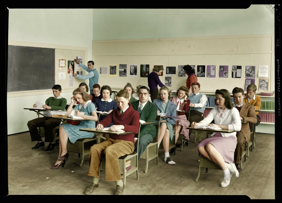 A classroom scene from the mid-20th century shows students sitting at desks, writing or reading, while two teachers stand near the blackboard and wall. The room is decorated with colorful portraits and educational materials.