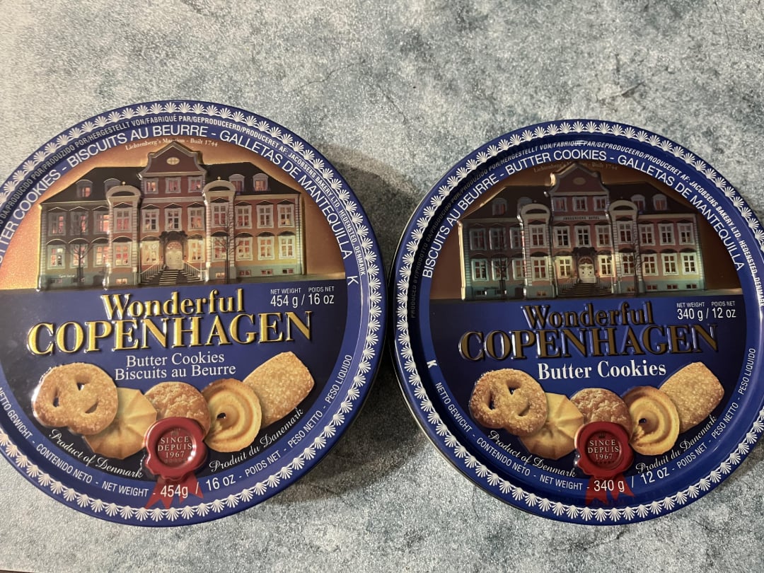 Two blue tins of Wonderful Copenhagen butter cookies, featuring an illustration of colorful buildings and various butter cookies on the front. The tin on the left is 454g, and the tin on the right is 340g.