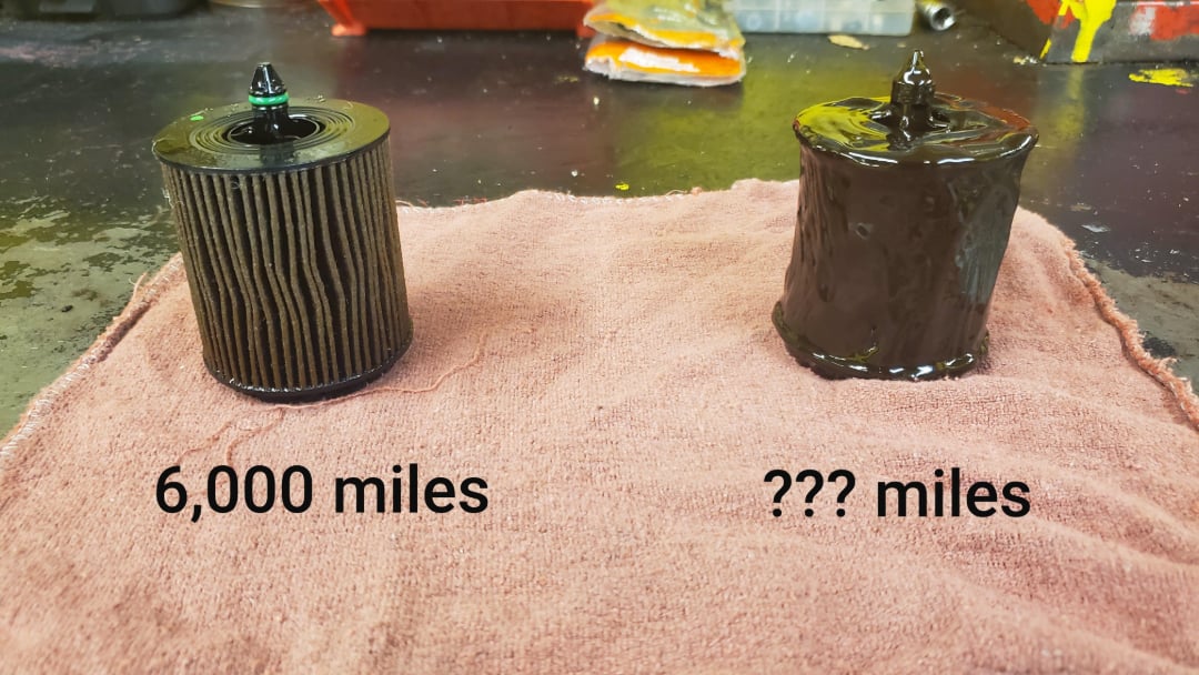 Two used oil filters on a pink cloth: the left filter is relatively clean and labeled "6,000 miles," while the right filter is heavily covered in black sludge and labeled "??? miles.