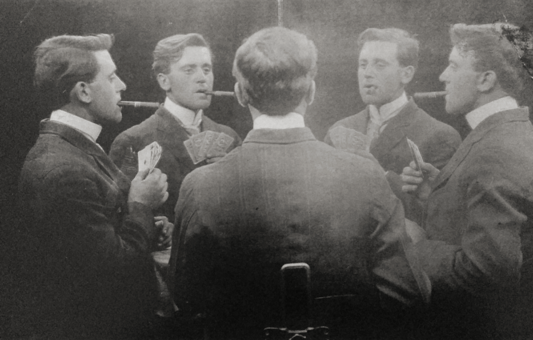 A man with a cigar holds playing cards, facing a mirror that reflects multiple images of himself, creating the illusion of several identical men in a circle.