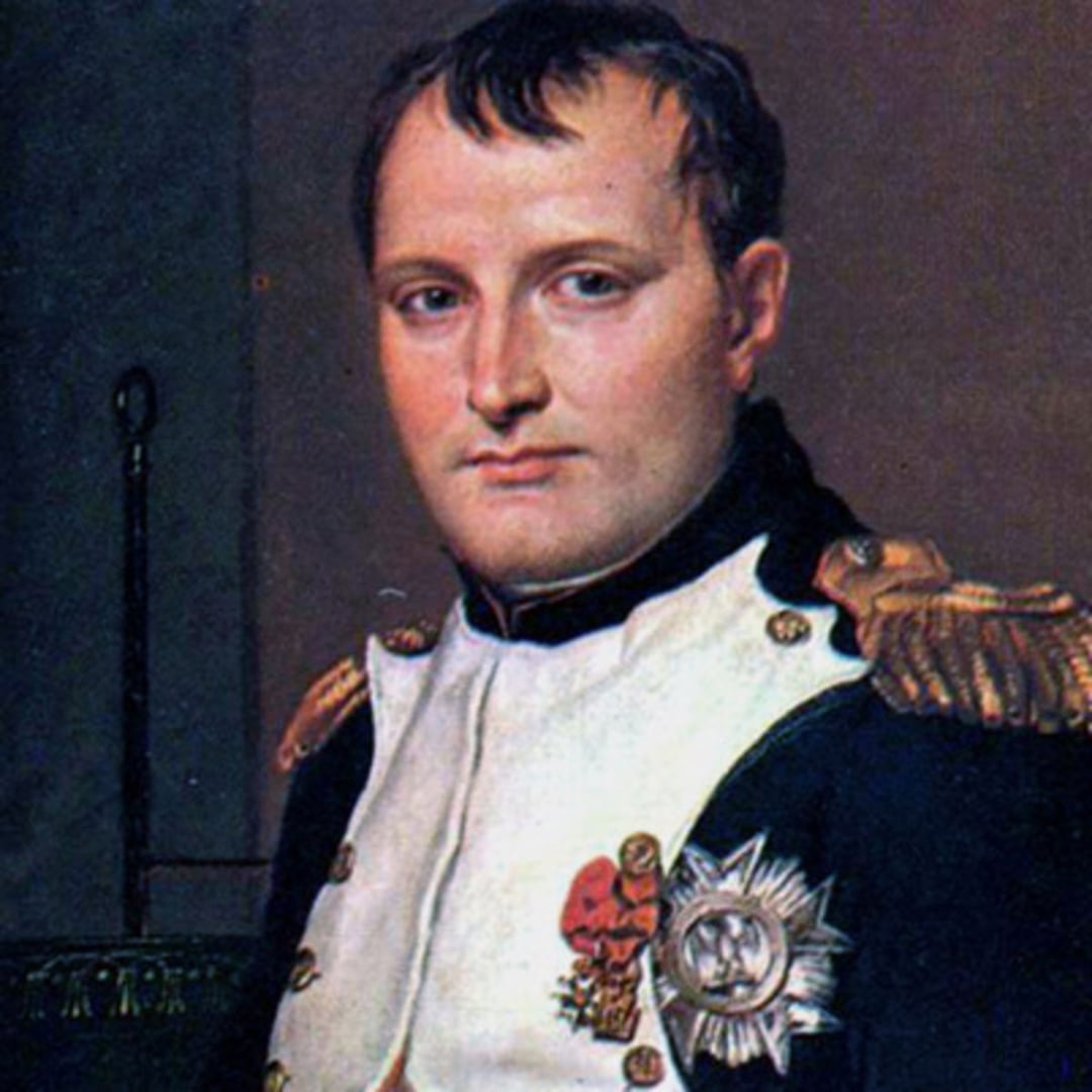 A man in a decorated military uniform with epaulettes and medals, wearing a white jacket with black trim, stands against a dark background, looking directly forward with a serious expression.