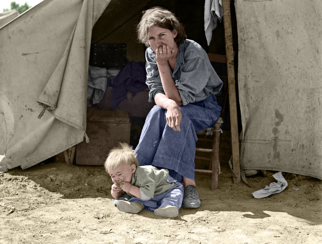 A woman sits on a chair outside a canvas tent, resting her chin on her hand, looking thoughtful. In front of her, a young child sits on the ground, appearing upset and crying.