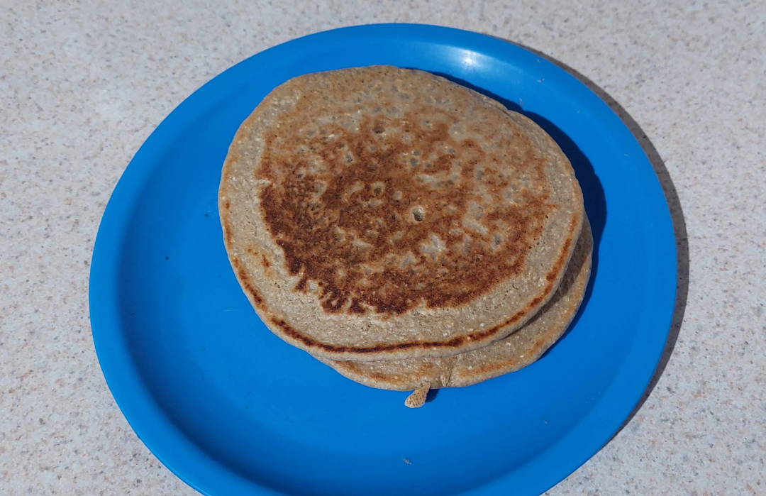 Two round, brown pancakes stacked on a bright blue plate, placed on a light-colored countertop.