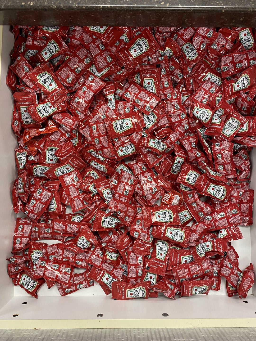 A large drawer filled with numerous red ketchup packets, all stacked and scattered on top of each other.