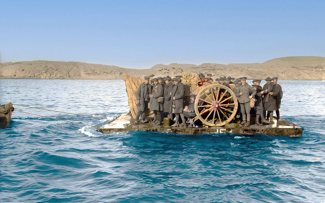 A group of men in coats and hats stand on a wooden raft carrying a large wagon wheel and other equipment, floating on blue water with rocky hills in the background under a clear sky.