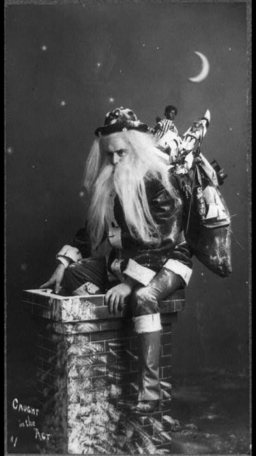 A man dressed as Santa Claus with a long white beard and a sack of toys is sitting on a chimney at night, with a crescent moon in the sky. The words “Caught in the Act” are written in the bottom left corner.
