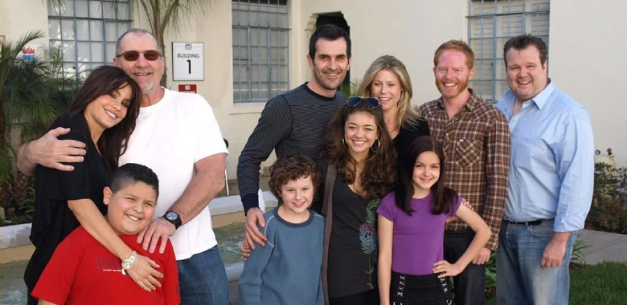 A group of adults and children stand smiling together outdoors in front of a building with large windows and a sign that says "Building 1." The group looks happy and relaxed, posing for the photo.
