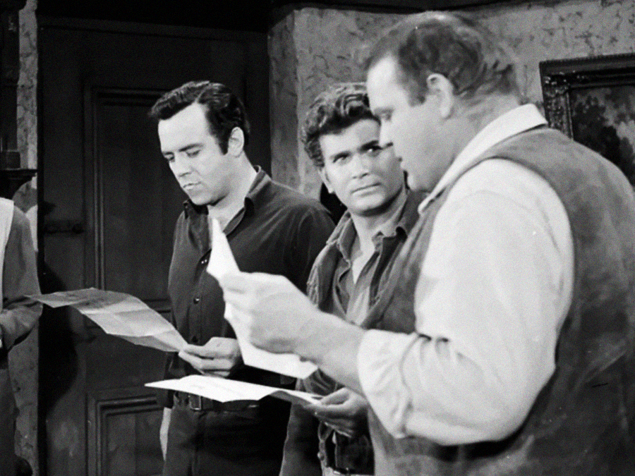 Three men in old-fashioned clothing stand indoors, reading papers with serious expressions. Two face forward while one is in profile. The scene appears to be from a black-and-white film or television show.