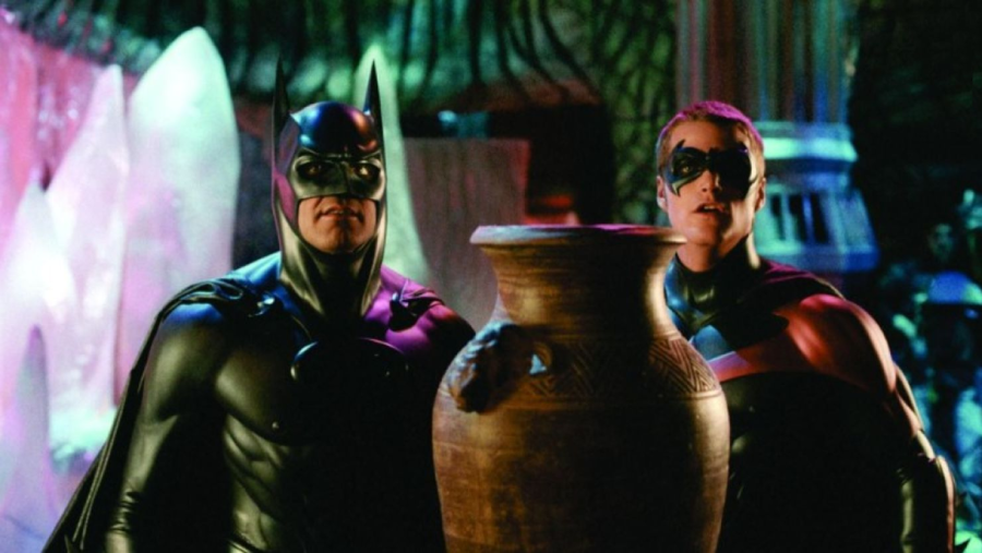 Batman and Robin, dressed in their superhero costumes, stand side by side in a colorful setting, looking ahead while holding a large, ornate clay vase between them.