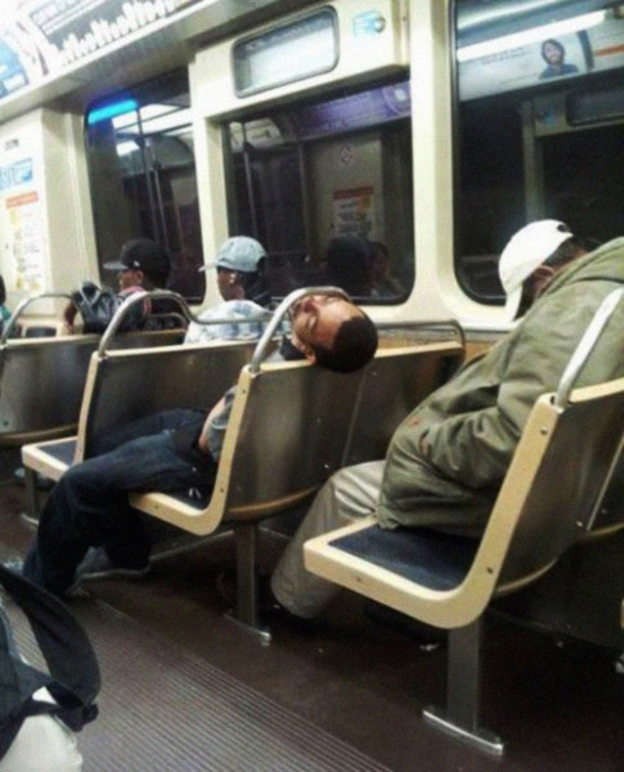 Several people are sleeping on a subway train; one man is slumped on a bench with his head tilted far back over the seat edge in an unusual, awkward position.