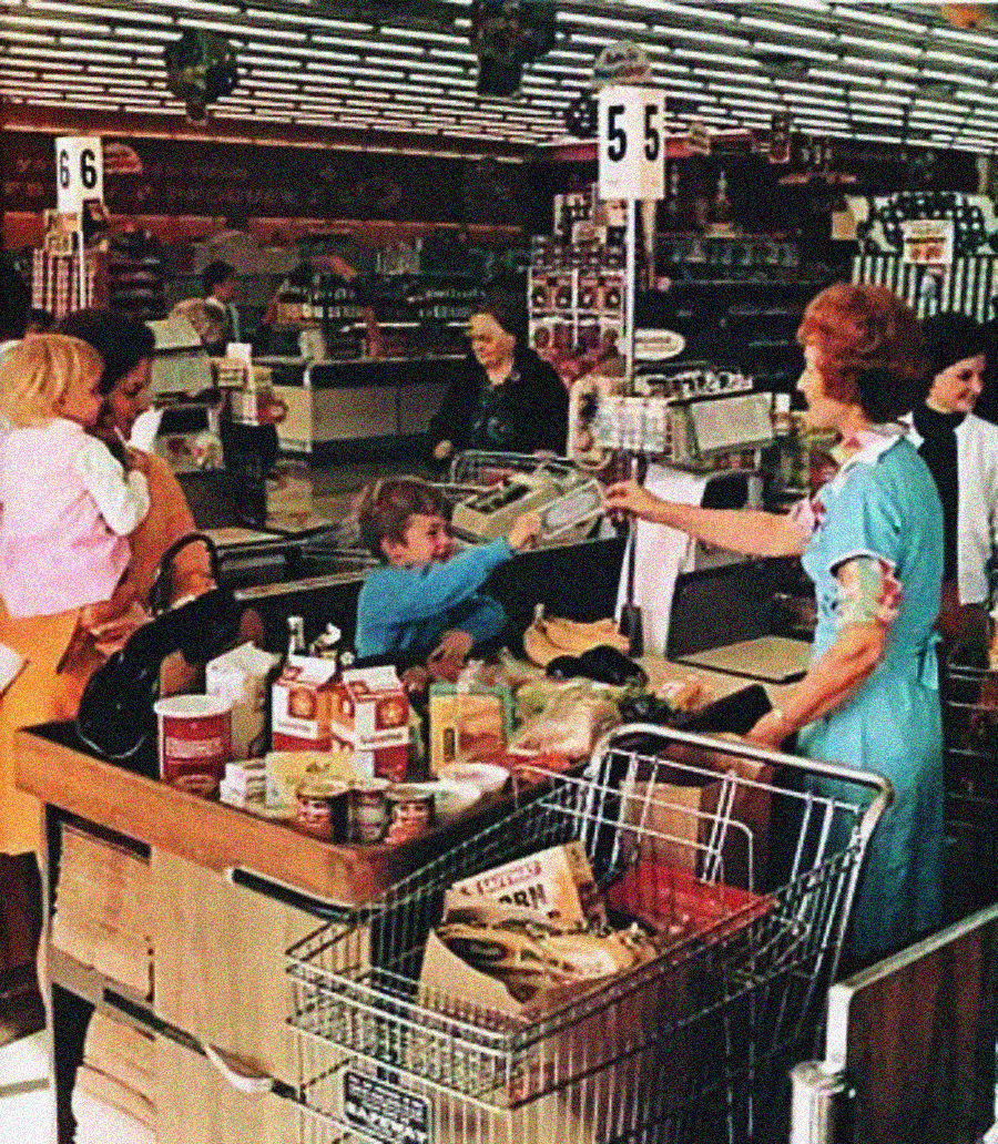 A vintage supermarket scene shows a cashier ringing up groceries while a young boy helps by handing over items. Two women and a young girl stand nearby, with full shopping carts and a variety of groceries on the counter.
