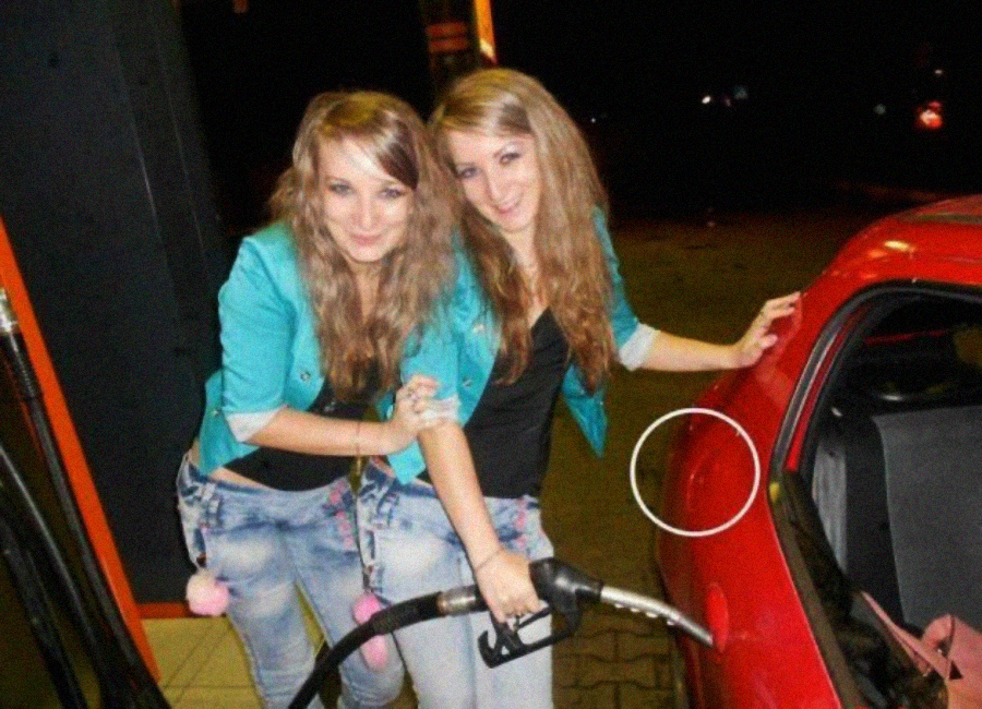 Two young women with long hair, both wearing teal jackets and jeans, stand close together at a gas station. One is pumping fuel into a red car. They are smiling and posing for the camera at night.