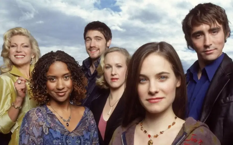 Six people stand outdoors under a cloudy sky, posing for the camera. Three women and three men, all dressed in casual to semi-formal attire, look directly at the viewer with neutral to slight smiles.