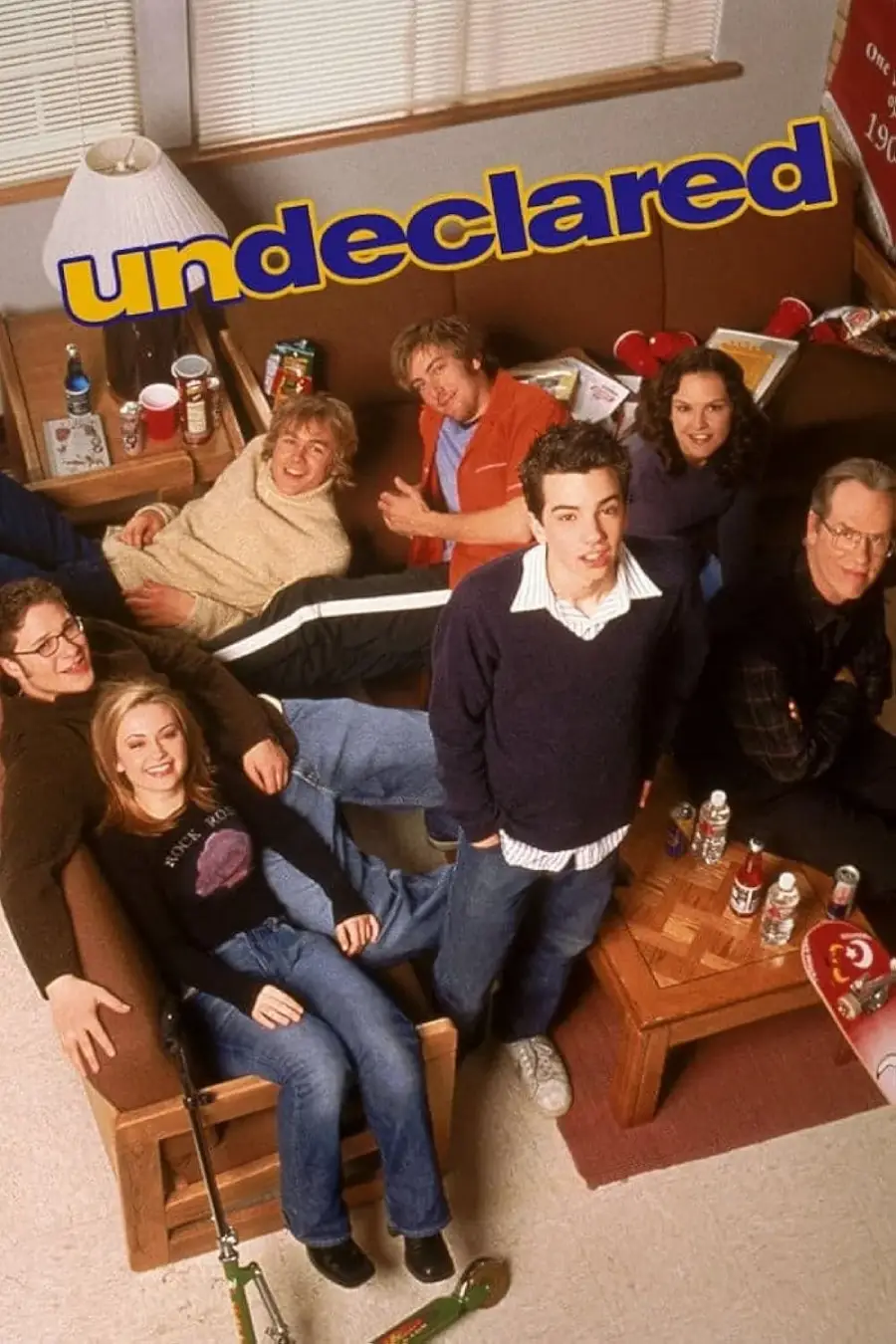 Seven young adults sit and lounge in a dorm room with snacks, drinks, and a ping pong paddle around them. The word “undeclared” is displayed in bold yellow letters above the group.