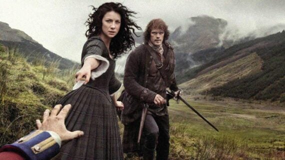 Claire and Jamie from Outlander standing together in the Scottish Highlands during sunset