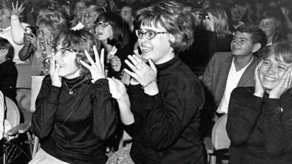 Excited fans screaming and reaching toward a celebrity during a live performance