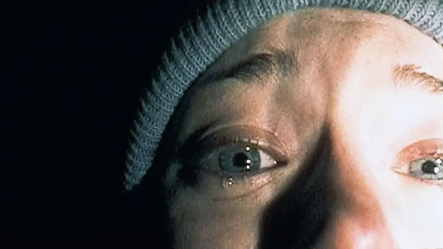 Close-up of a person's tearful face, wearing a knit cap, illuminated by harsh light in a dark setting. Only their eyes, nose, and part of their forehead are visible.