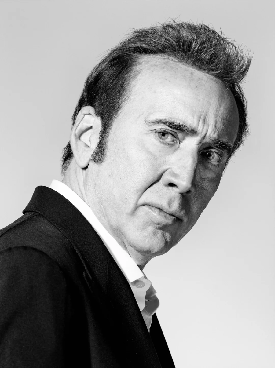 A man in a suit with short hair looks seriously at the camera in this black and white portrait, set against a plain light background.