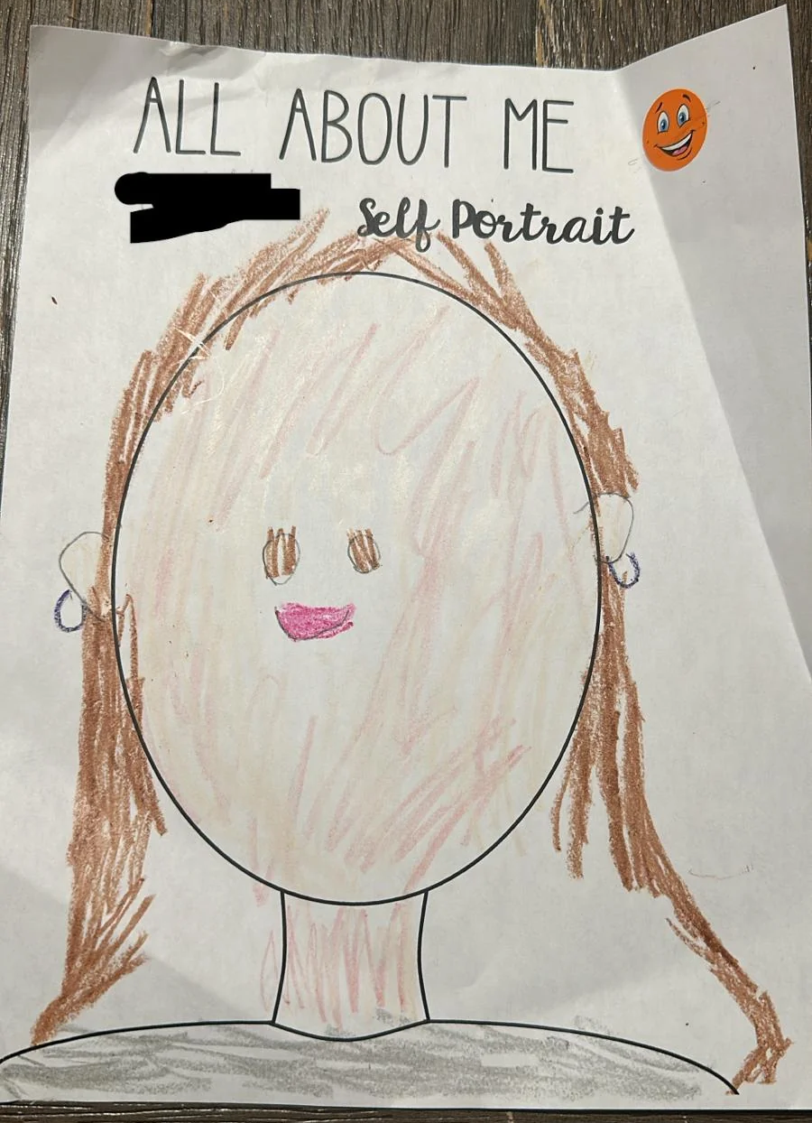 A child’s drawing of a self-portrait features a round face with brown hair, pink lips, and small earrings on a white paper titled “ALL ABOUT ME Self Portrait.” A smiley face sticker is in the top right corner.