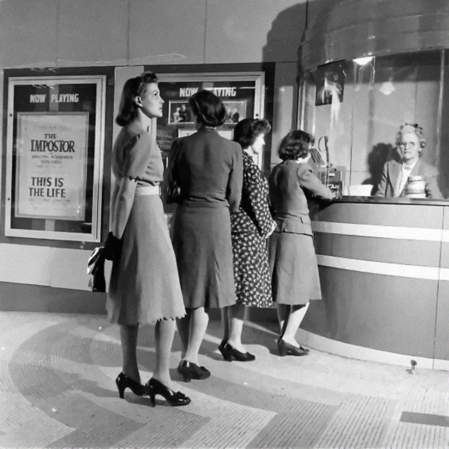 Four women stand in line at a movie theater ticket booth, with a smiling cashier behind the glass. Movie posters for "The Impostor" and "This Is the Life" are visible on the wall. The scene appears vintage.