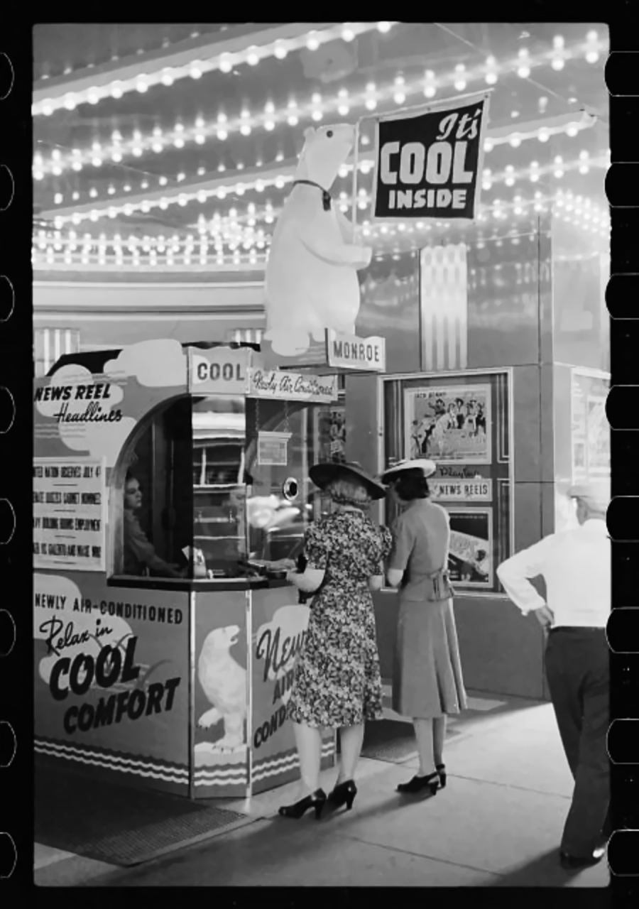 Two women in 1940s attire stand at a ticket booth outside a theater with a large polar bear figure and a sign reading "It's COOL inside," advertising air conditioning. Bright marquee lights are overhead.