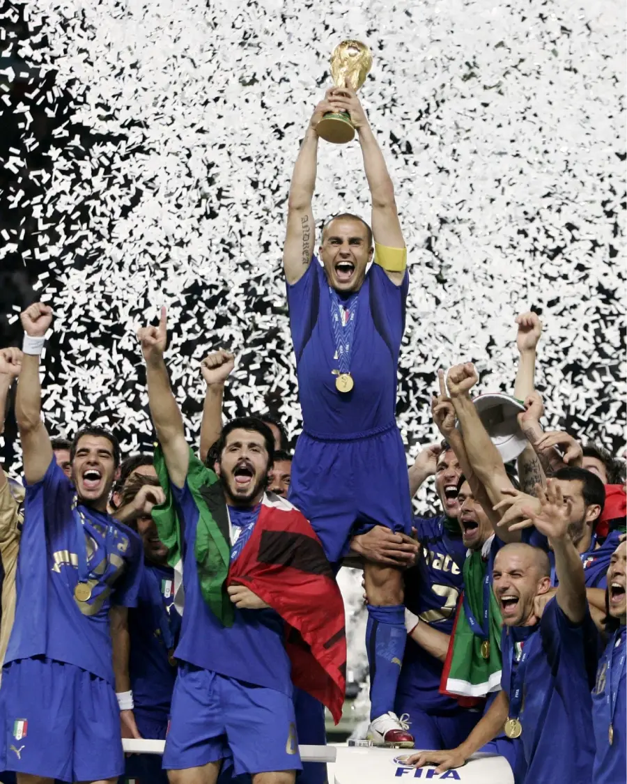 A soccer team in blue uniforms celebrates as their captain lifts the FIFA World Cup trophy. Confetti falls around them, and players cheer with excitement, some holding flags and medals.