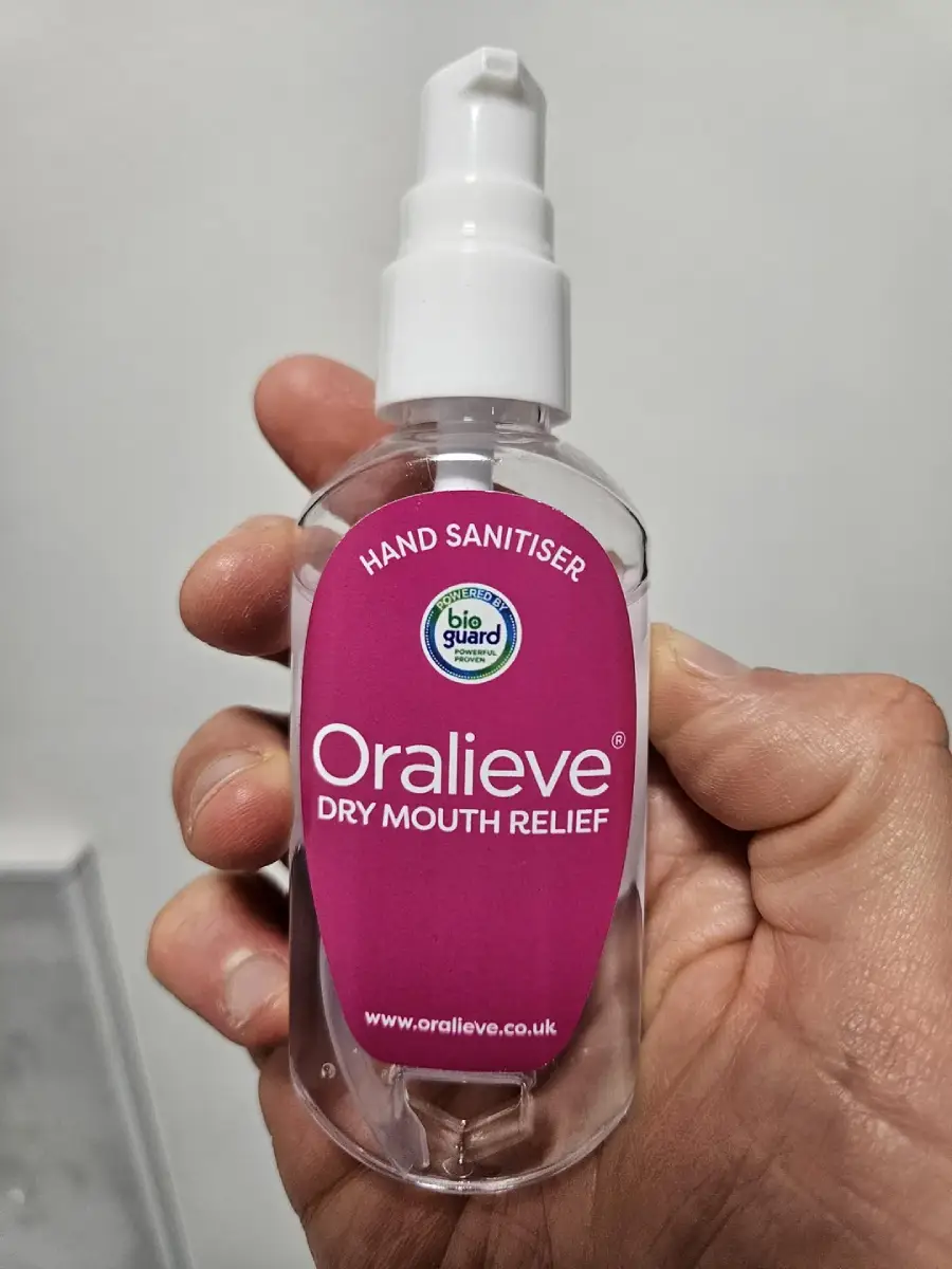 A hand holding a clear spray bottle labeled "Oralieve Dry Mouth Relief," with "Hand Sanitiser" printed at the top and a "Bio Guard" logo above the main label. The background is plain and light-colored.