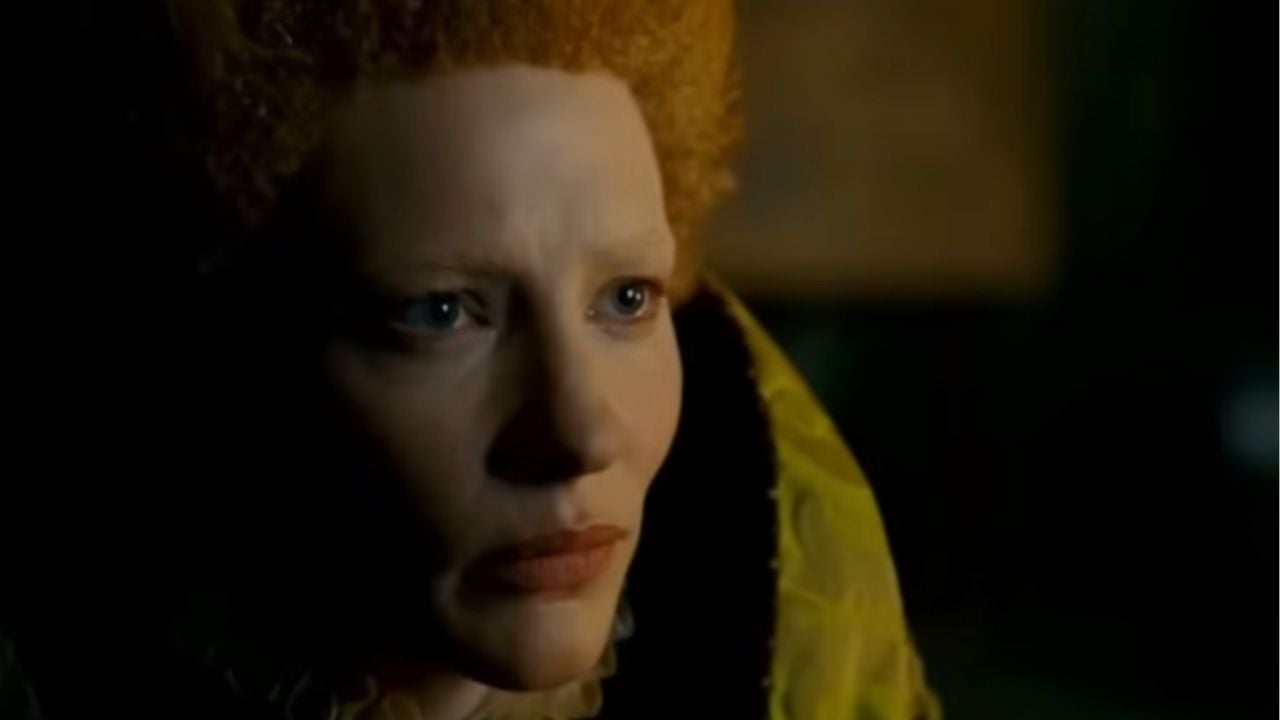 A person with pale skin, red curly hair, and period costume stares intensely forward, lit dramatically from the side.