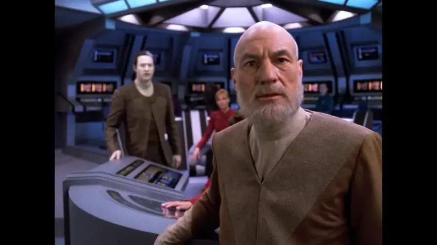 An older man with a white beard and futuristic clothing stands on a spaceship bridge, looking ahead with concern. Two others, one pale-skinned, stand behind him at control panels, with a blue-lit sci-fi background.