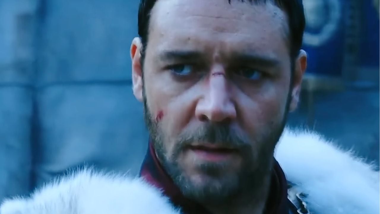 A man with short dark hair and facial scars wears a white fur cloak and looks serious against a blue stone background.
