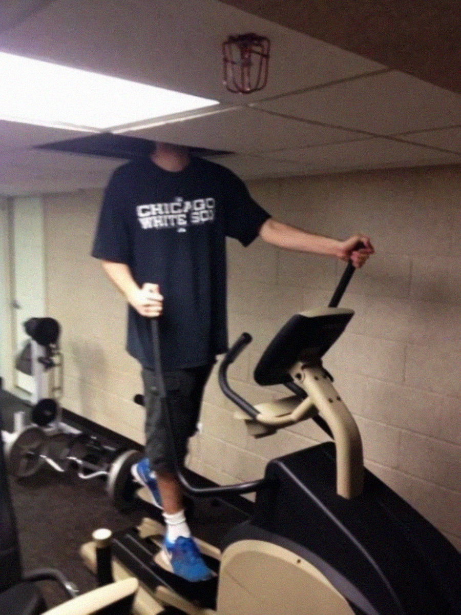 A very tall person using an elliptical machine in a gym, with their head poking through a ceiling tile due to their height, making their face not visible.