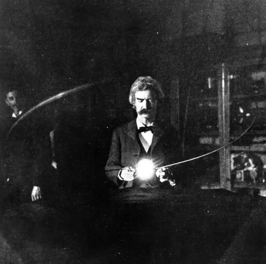A black and white photo of a man in a suit holding a glowing object, likely an early electric lamp, in a dark room filled with scientific equipment.