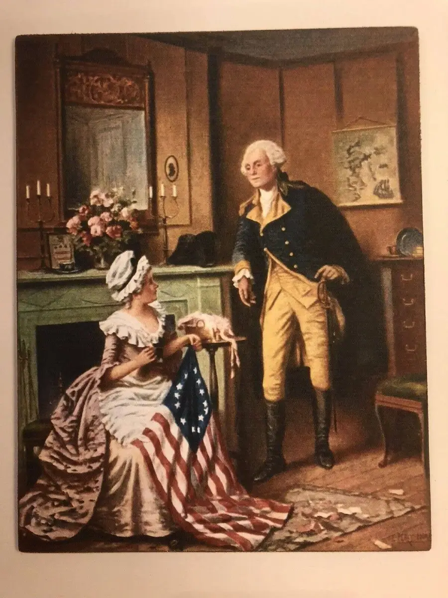 A woman in colonial-era clothing holds a partially sewn American flag while seated. A man in Revolutionary War attire stands nearby, appearing to speak to her. They are indoors with a fireplace and patriotic decor.