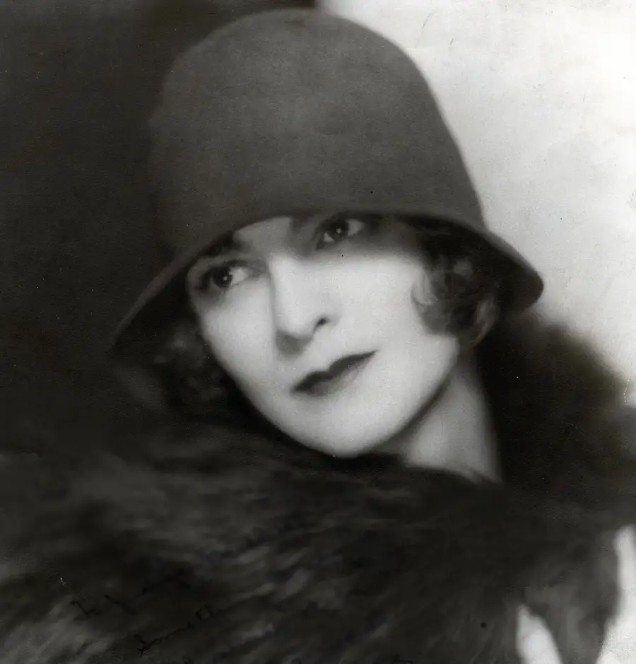 Black-and-white portrait of a woman wearing a cloche hat and a dark fur stole, with short wavy hair and a soft, thoughtful expression, looking slightly away from the camera.