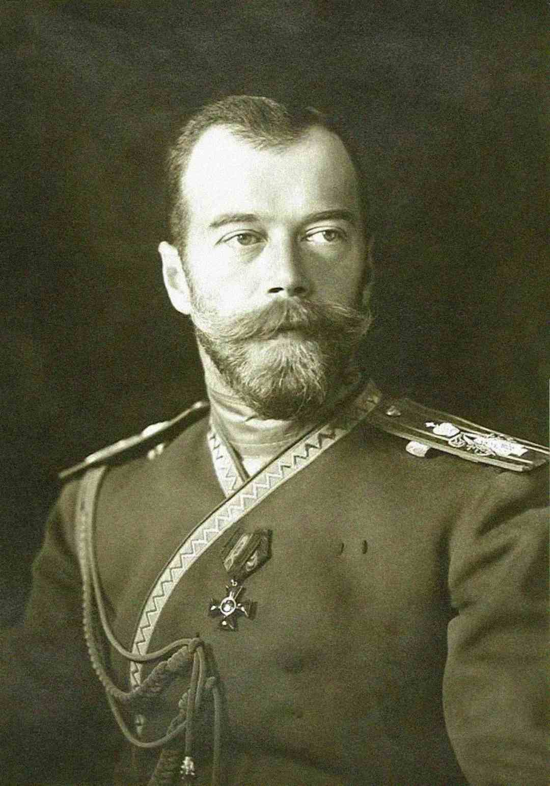 A sepia-toned portrait of a man with a beard and mustache, wearing a military uniform adorned with medals and decorative shoulder cords, looking slightly to the side against a dark background.