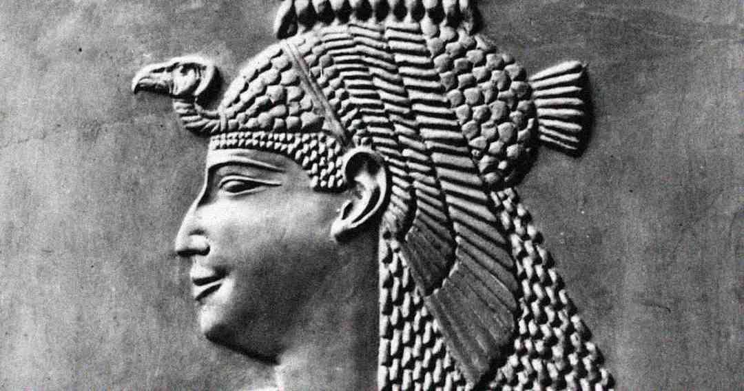 Ancient stone relief of a woman in profile, wearing an elaborate headdress featuring a cobra and detailed braids, symbolizing royalty in ancient Egypt.